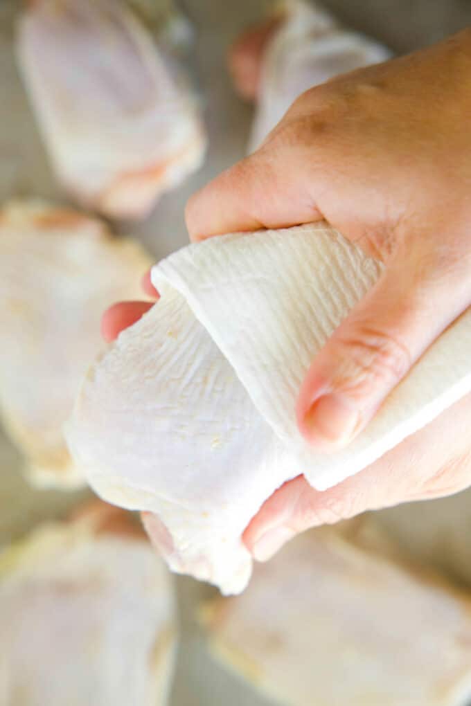 Hands using paper towels to pat raw chicken thighs dry.