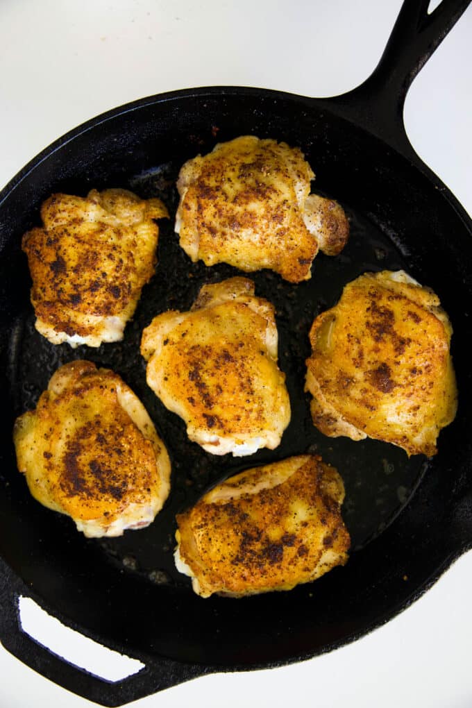 An overhead look at chicken thighs being seared in a cast iron skillet.