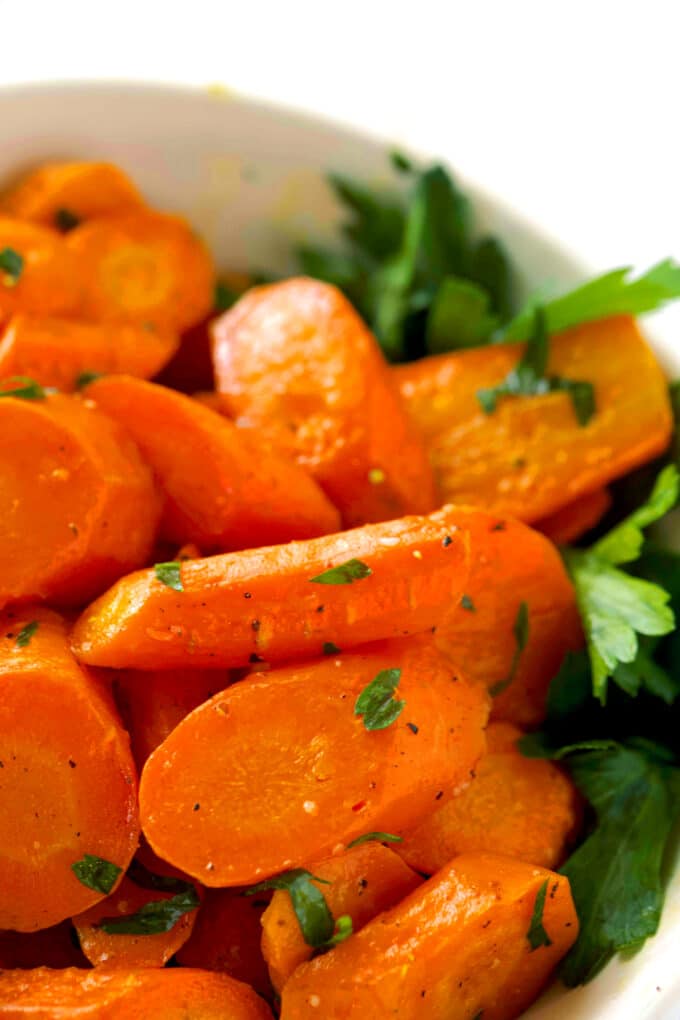 A close up of Roasted Carrots in a bowl, with a parsley garnish.