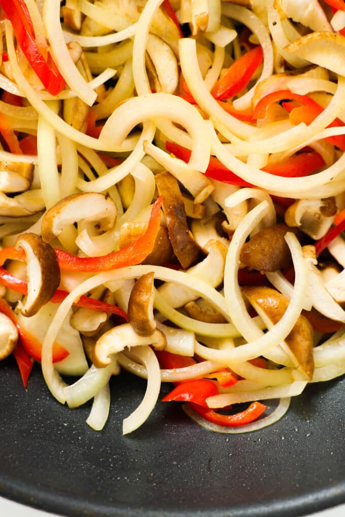 Onion, peppers, and mushrooms being sautéed together in a pan with oil.