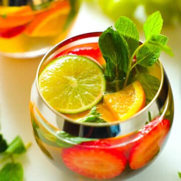 A close up, overhead view of a stemless wine glass of White Wine Sangria with a mint garnish.