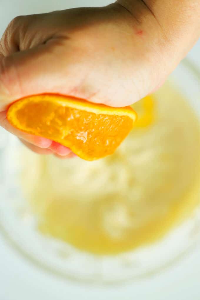 A hand squeezing half of an orange over the bowl of cream cheese and marshmallow fluff.