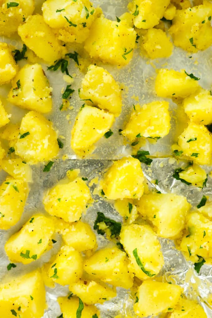 The raw potato cubes, coated in seasoning and oil, spread out on the pan and ready to bake.