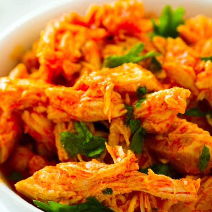 A close up of Crockpot Buffalo Chicken shredded up in a bowl with a chopped herb garnish.