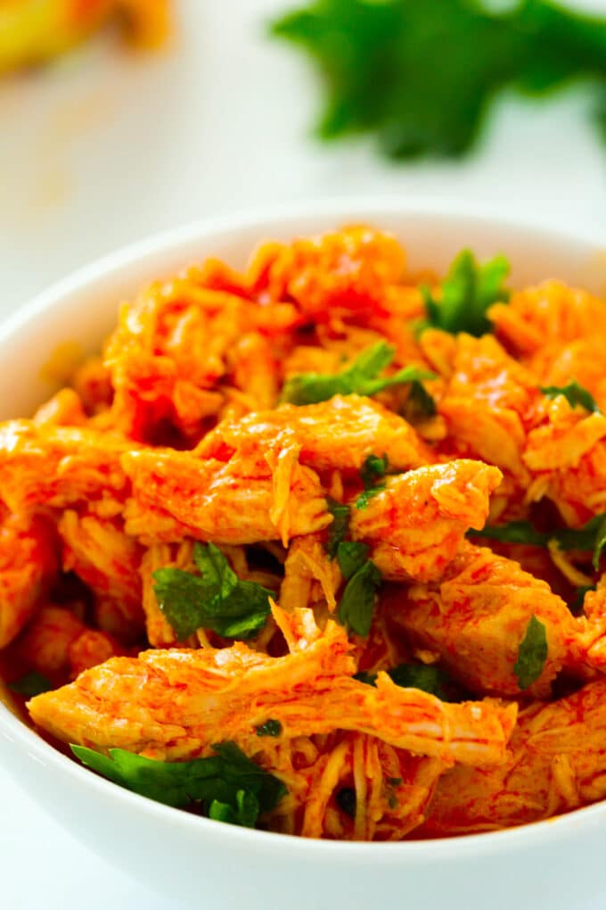 A close up of Crockpot Buffalo Chicken shredded up in a bowl with a chopped herb garnish.