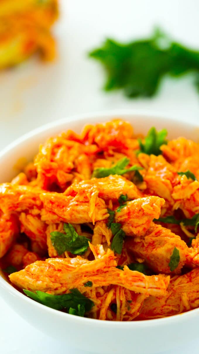 A close up of Crockpot Buffalo Chicken shredded up in a bowl with a chopped herb garnish.