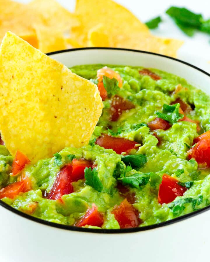 A close up of a bowl of Guacamole with a big tortilla chip stuck into it.