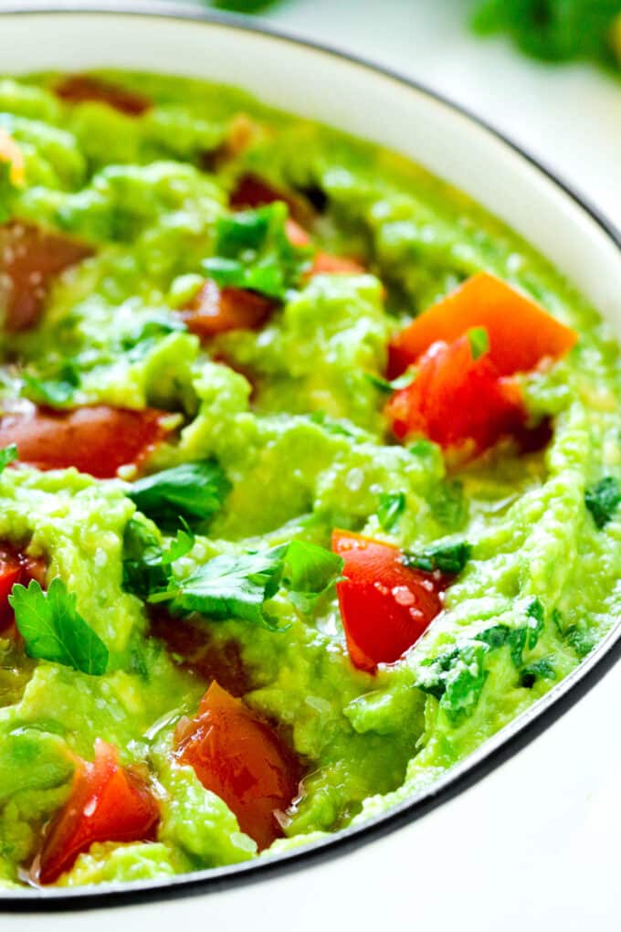 A close up of a bowl of Guacamole. It is a beautiful green color with a pop of red from the tomatoes.