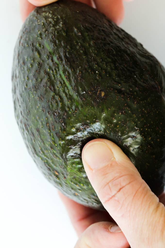 Hands gently squeezing an avocado to check the ripeness.