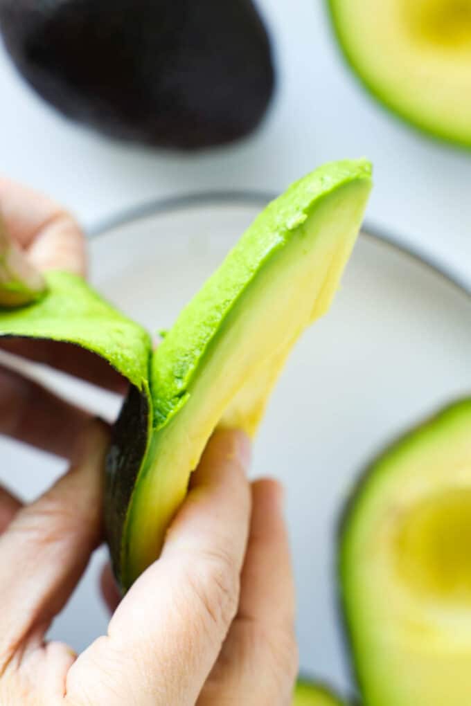 Hands peeling the peel off of a quarter of avocado.