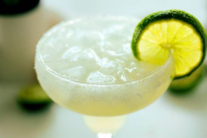 A close up of a Homemade Margarita in a margarita glass with a lime wheel on the edge and a salt rim.