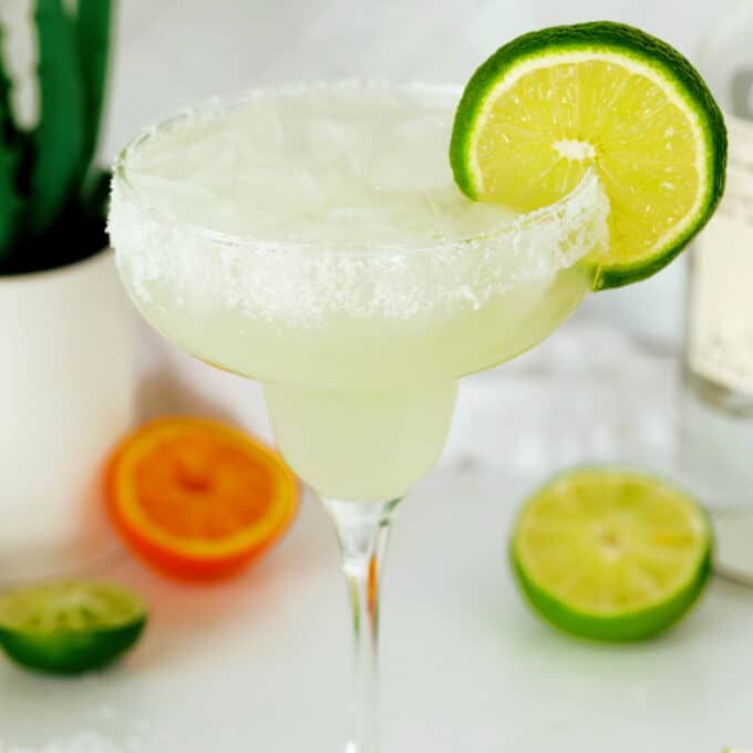 A Homemade Margarita in a classic margarita glass with a lime wheel on the side and a salt rim. The drink is a very light green.