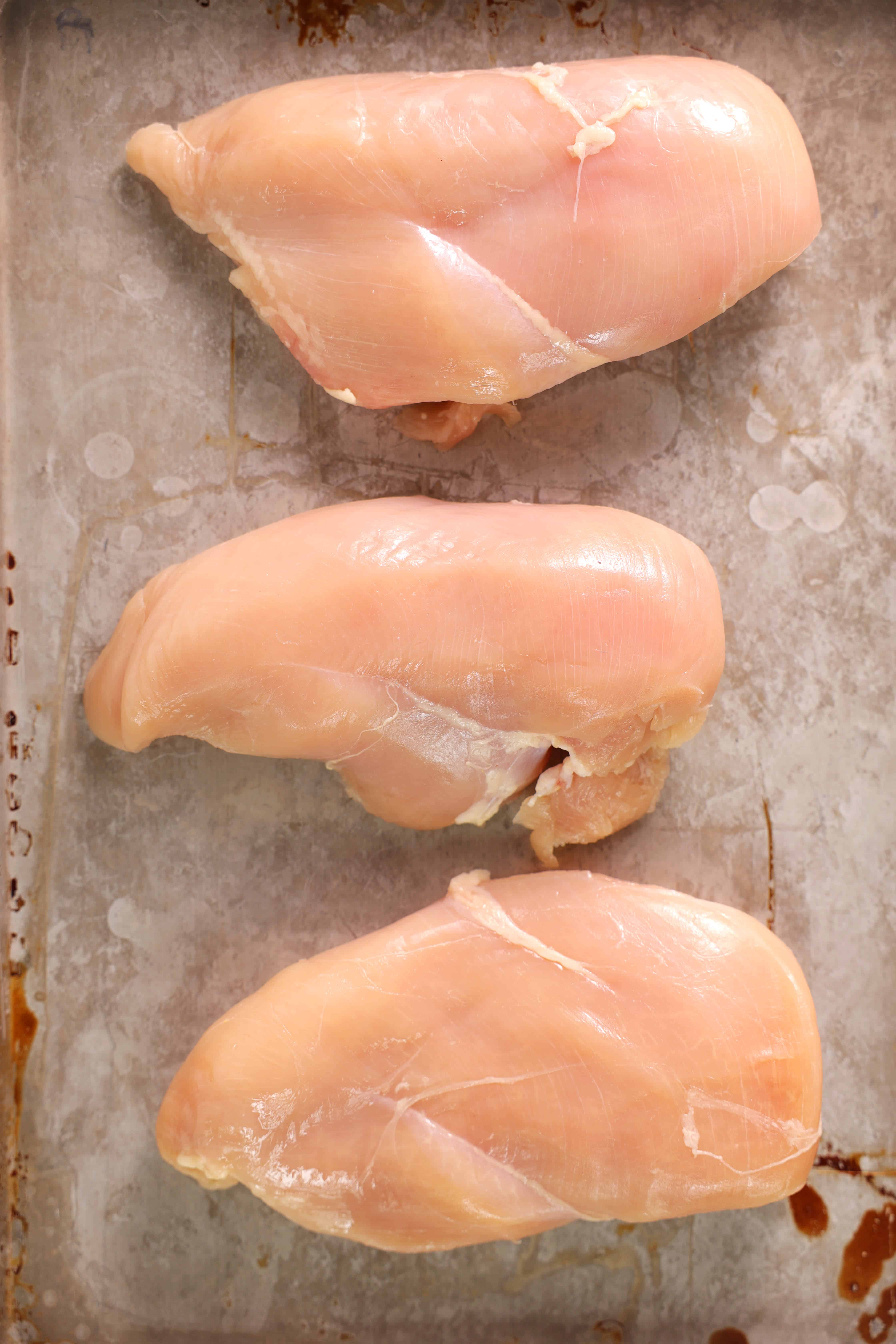 An overhead shot of three raw chicken breasts on a sheet pan. 