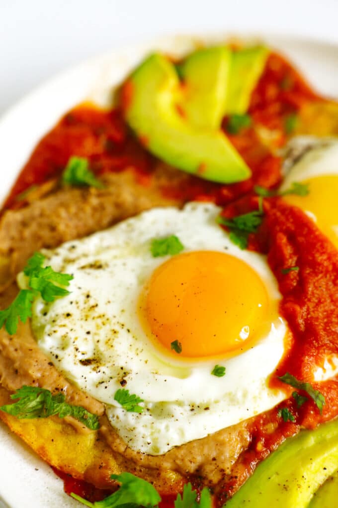 A close up of Huevos Rancheros on a plate with slices of avocado.