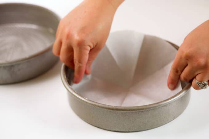 Hands putting down a round piece of parchment into the bottom of a cake pan.