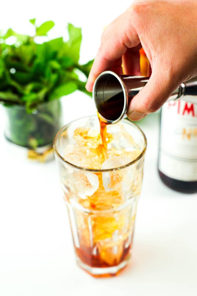 Pimm's gin liqueur being poured into a tall glass of ice, from a jigger.