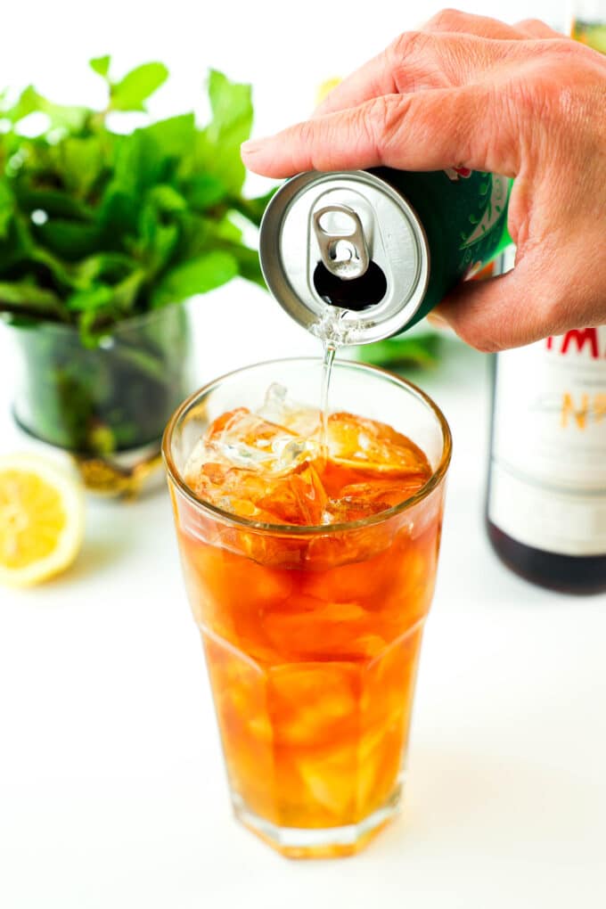 A can of ginger ale being poured into the glass of ice, Pimm's, and lemon juice.