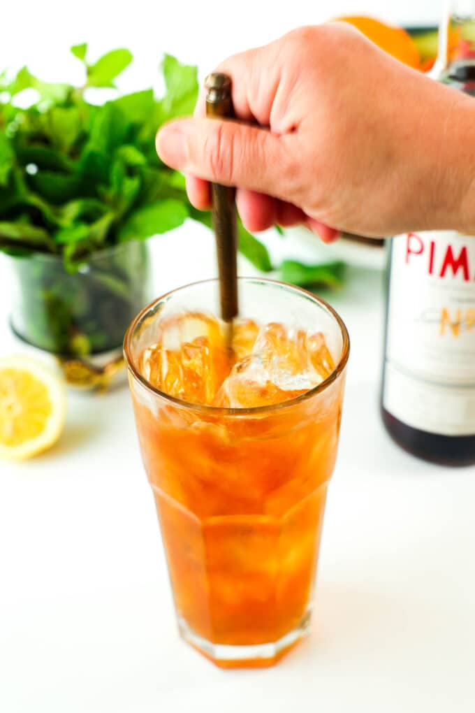A hand using a long spoon to stir the Pimm's Cup before adding the fruit.