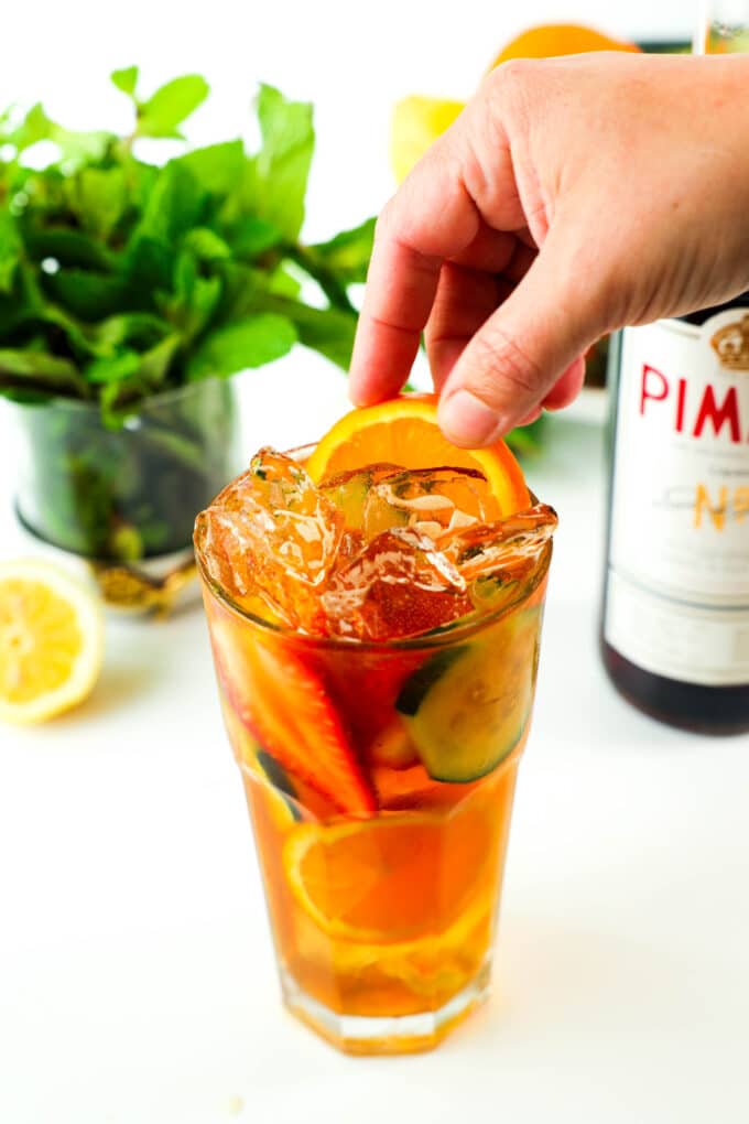 A hand adding slices of fruit to the Pimm's Cup cocktail.