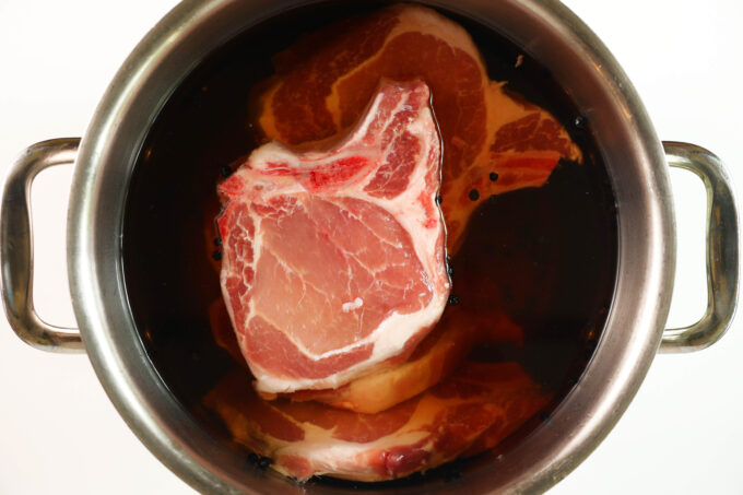 An overhead view of raw pork chops in a brine in a large pot.