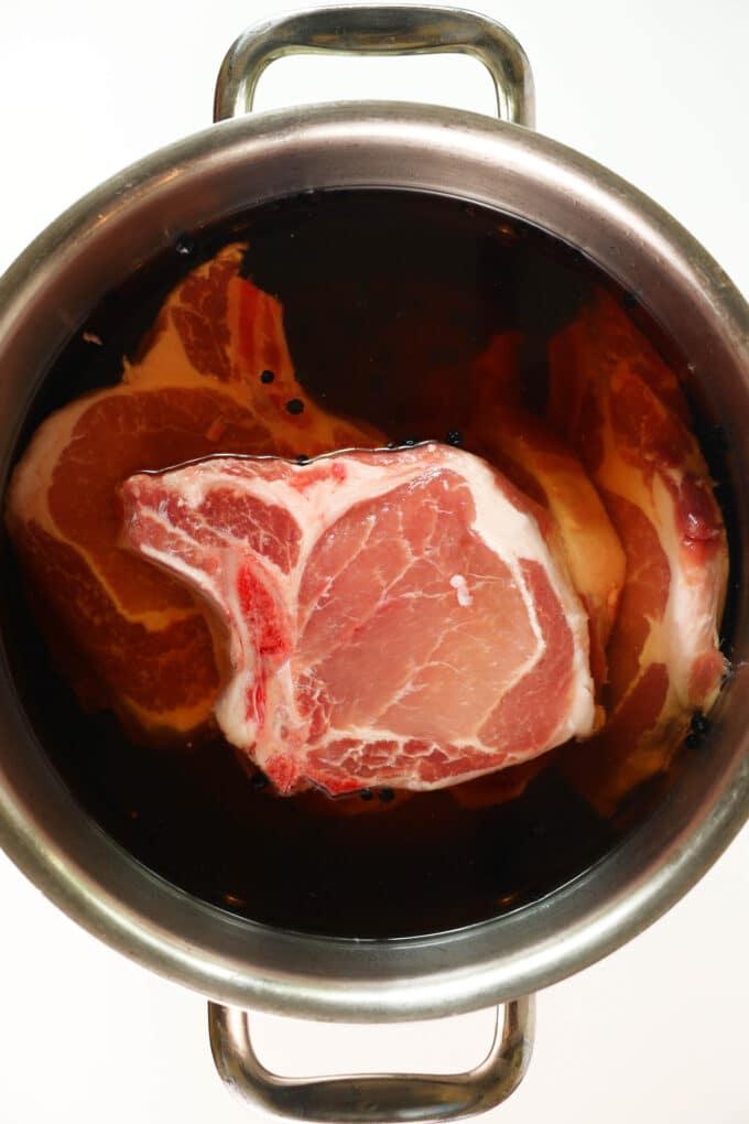 An overhead view of raw pork chops in a brine in a large pot.