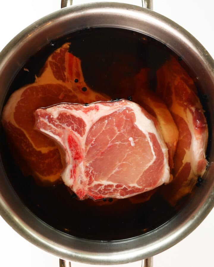 An overhead view of raw pork chops in a brine in a large pot.