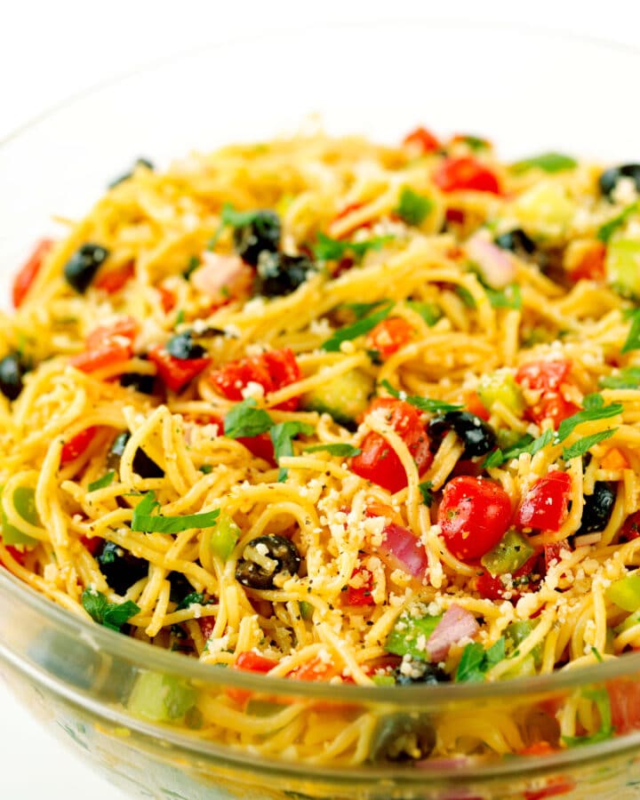 A close up shot of a clear glass bowl filled with spaghetti salad.