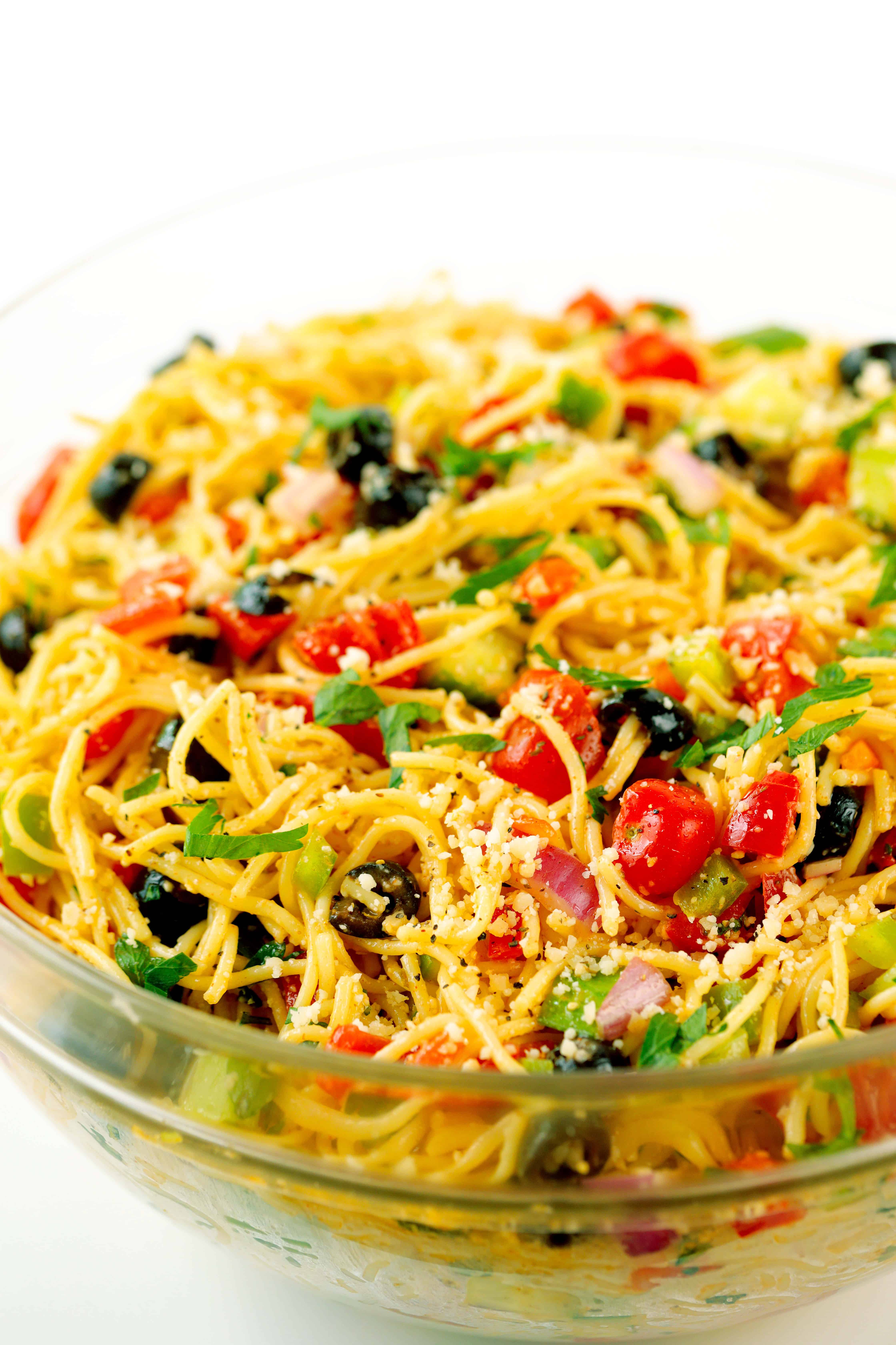 A close up shot of a clear glass bowl filled with spaghetti salad. 
