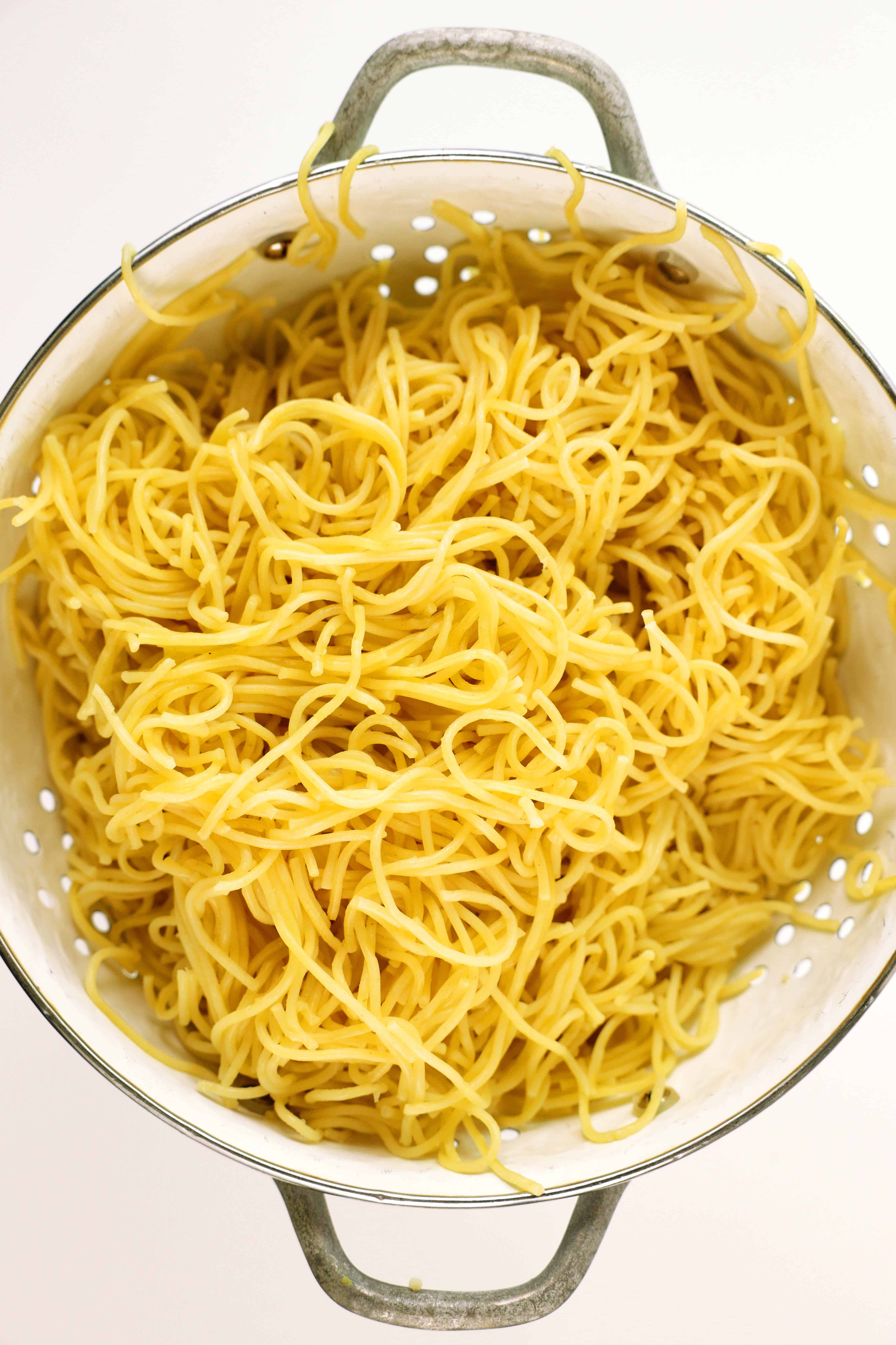 A vertical overhead photo of a white colander filled with spaghetti noodles. 