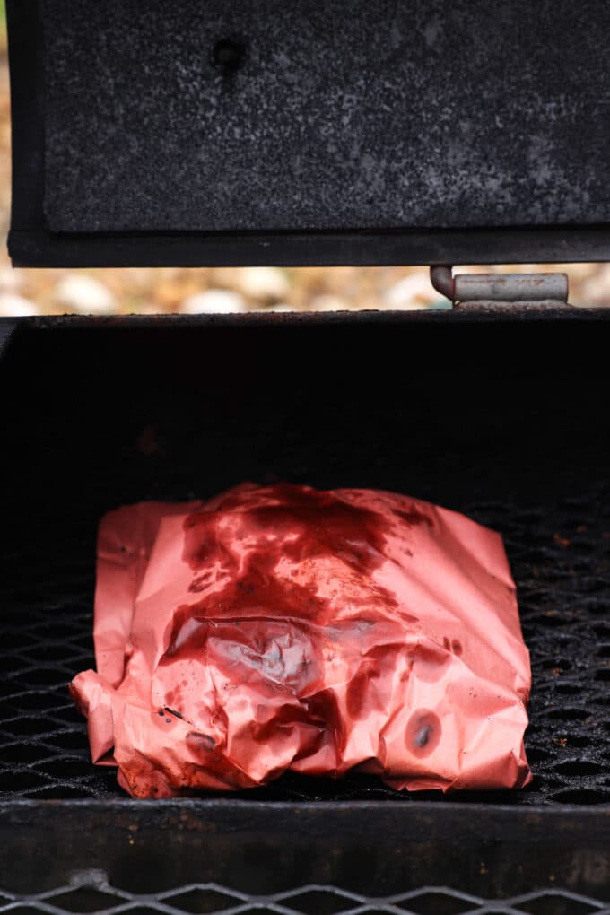 Beef Ribs completely wrapped up in butcher's paper in a smoker.