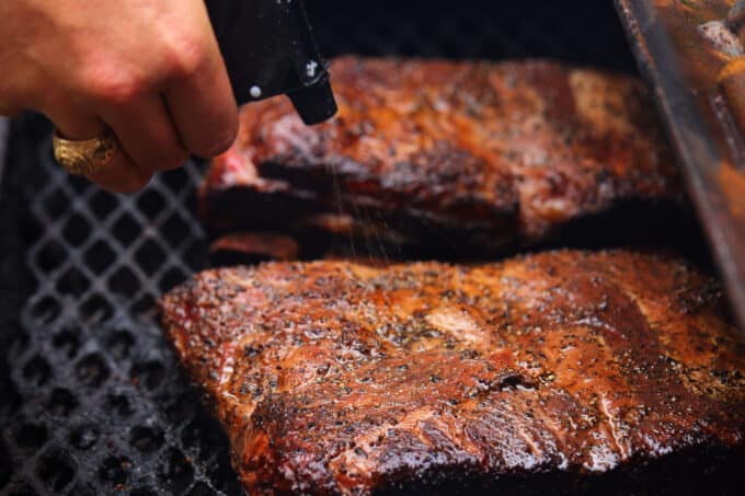 A hand spritzing the Beef Ribs in the smoker with a spray bottle.