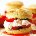 A close up of a Strawberry Shortcake Biscuit that has been cut in half and has strawberry filling and whipped cream in between the two pieces.