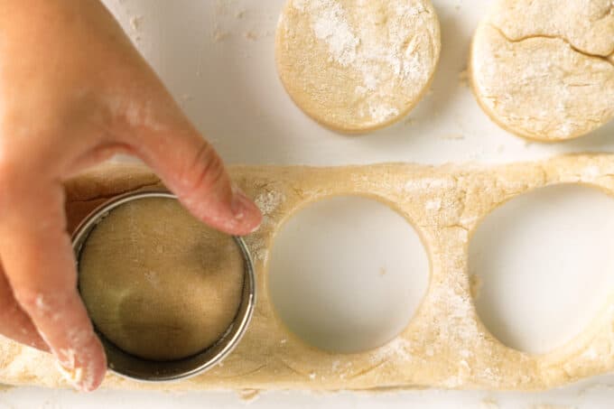 A hand using a biscuit cutter to punch circles out of the flattened dough.