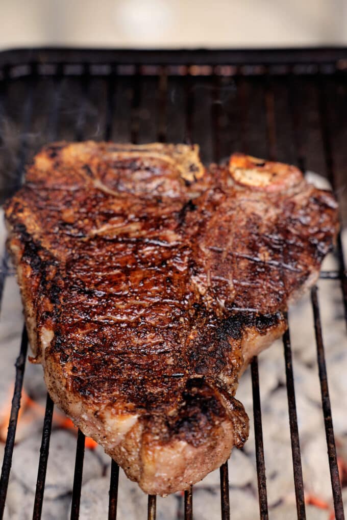 A T-bone Steak cooking on a charcoal grill.
