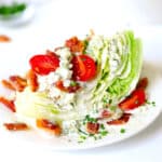 A close up of a Wedge Salad with sliced grape tomatoes, pieces of crispy bacon, blue cheese dressing, and blue cheese crumbles on top.