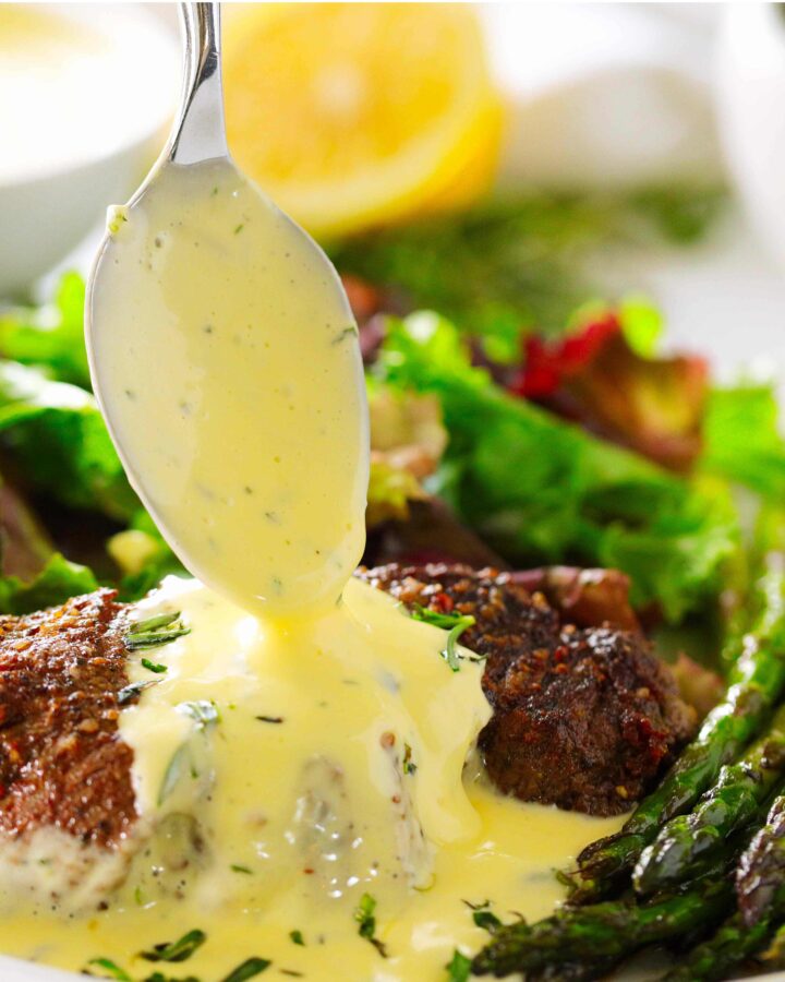 Bearnaise Sauce being spooned over a steak on a plate with a salad and asparagus.