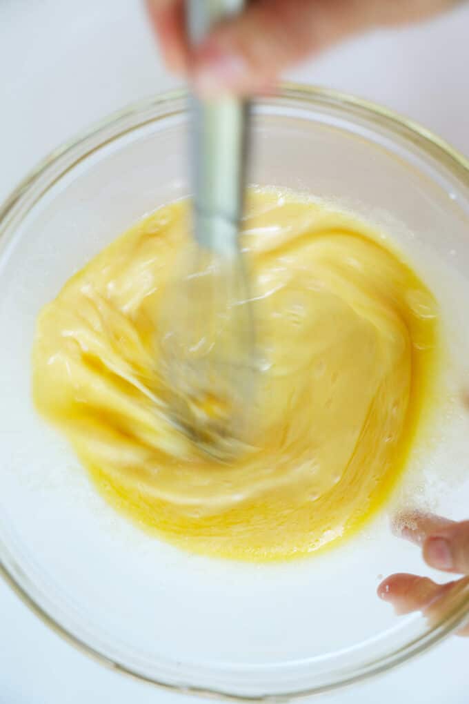 The egg and butter mixture being whisked together in a large glass mixing bowl.