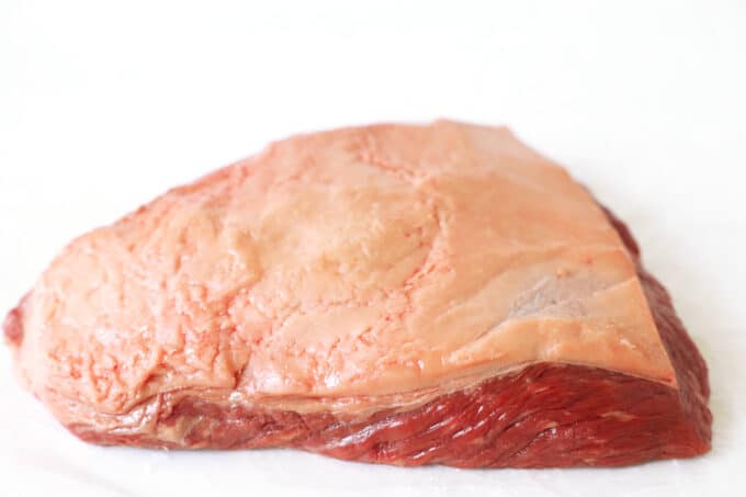 A raw roast with a fat cap on the top sitting on a white surface.