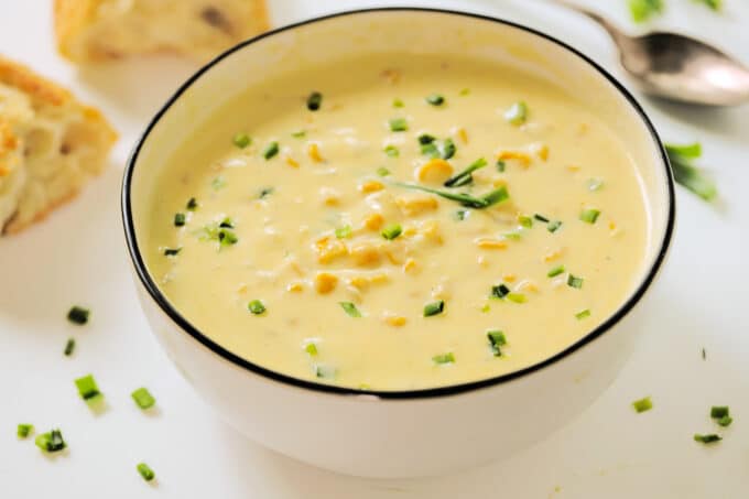 A bowl of Cream Corn Soup with chopped chives on top and a couple pieces of crusty bread nearby.