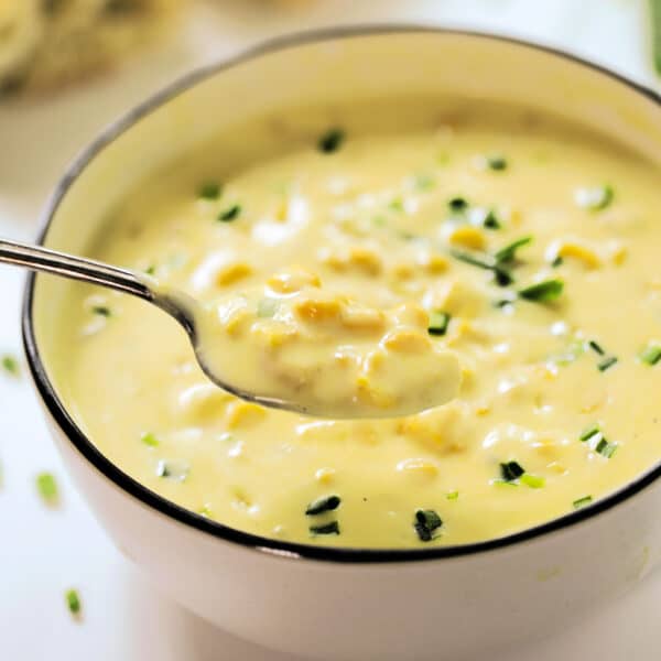 A spoon taking a scoop out of a bowl of Cream Corn Soup with chopped chives on top.