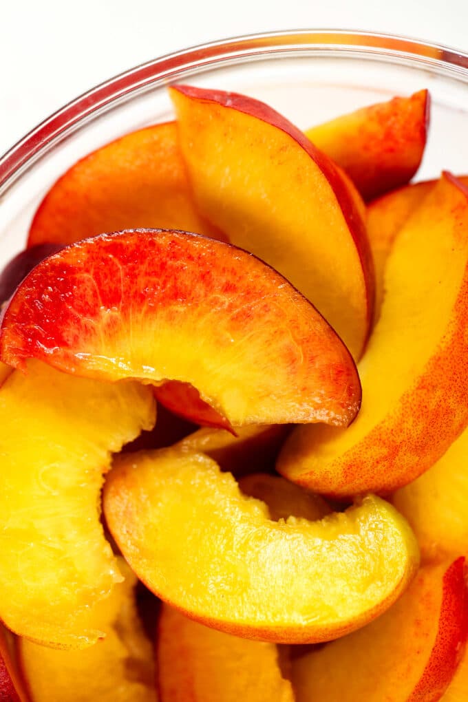 A close up look at slices of fresh peach in a glass bowl.