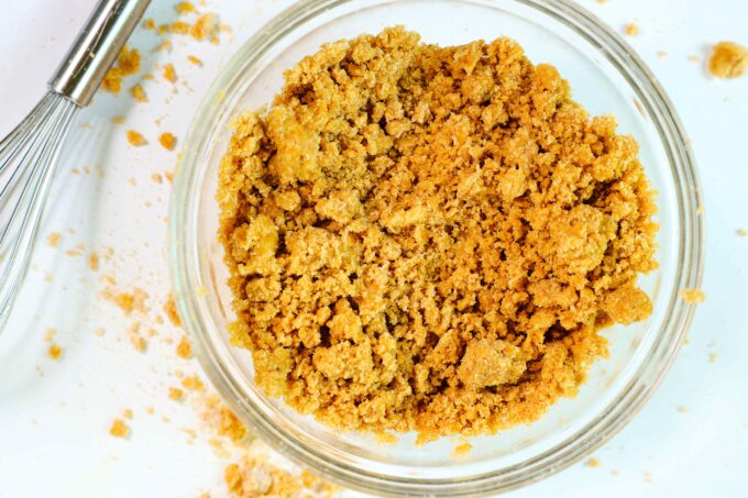 An overhead look at the crumble topping in a mixing bowl with a whisk and some crumbs on the counter nearby.