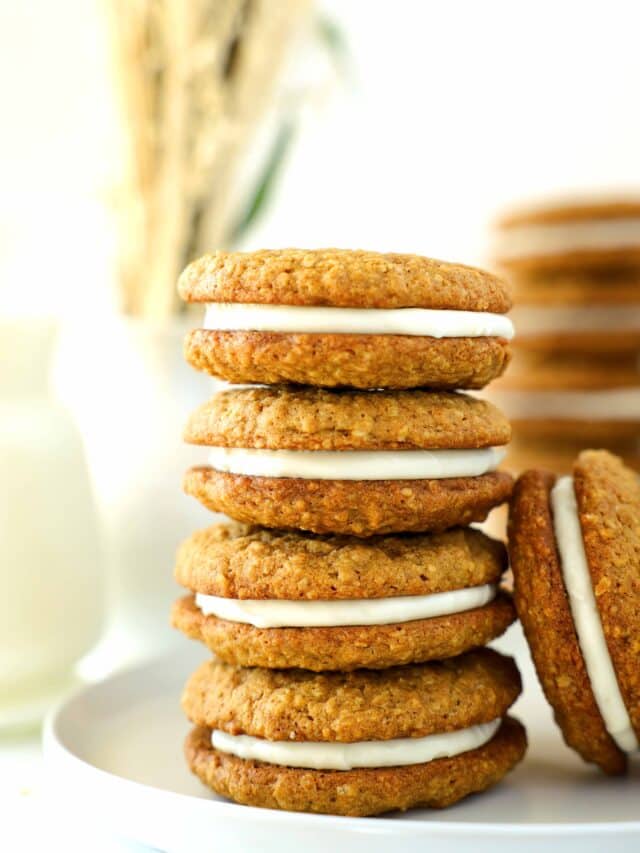 A tall stack of Oatmeal Cream Pies sitting on a white plate with one more leaning against the side of the stack.