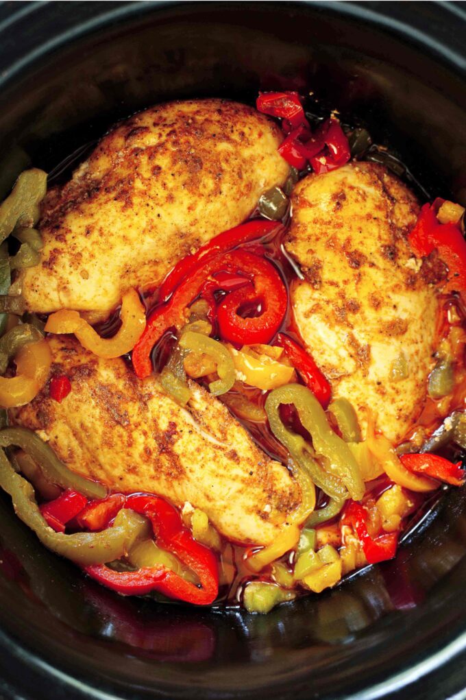 An overhead look into a crockpot of cooked chicken breasts, onions, and bell peppers.