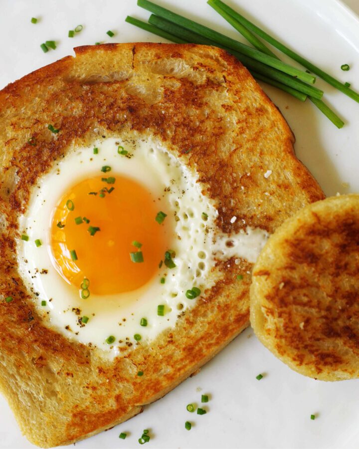 An overhead shot of Eggs in a Basket on a white plate with chives sprinkled on top and some laying the side of the plate.