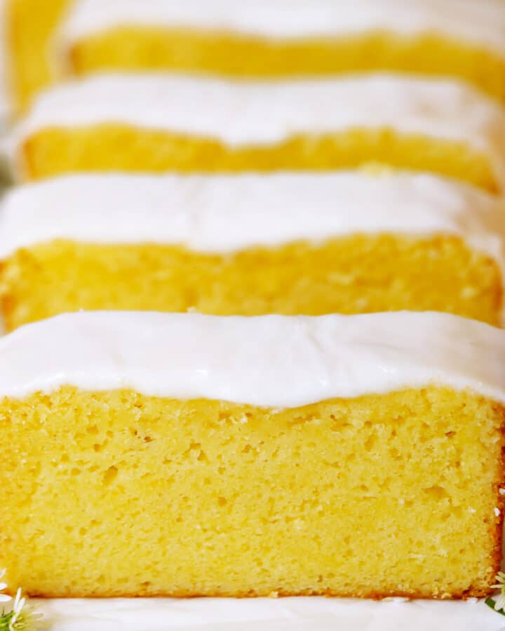 Several slices of Lemon Pound Cake lined up in a row. The cake is very yellow with a bright white glaze on top.