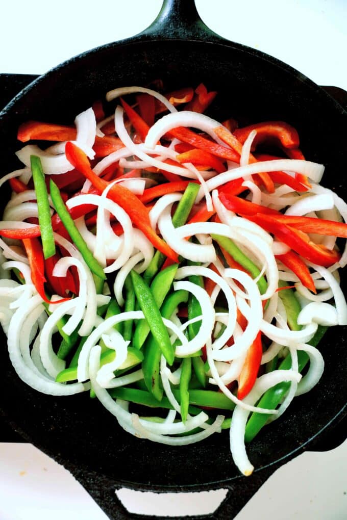 Raw onion and red and green bell peppers that have been sliced up are all mixed together in a cast iron skillet.