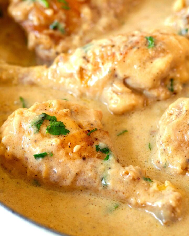 Smothered Chicken legs still in the pan. The chicken is in a brown gravy with a chopped parsley sprinkled on top.