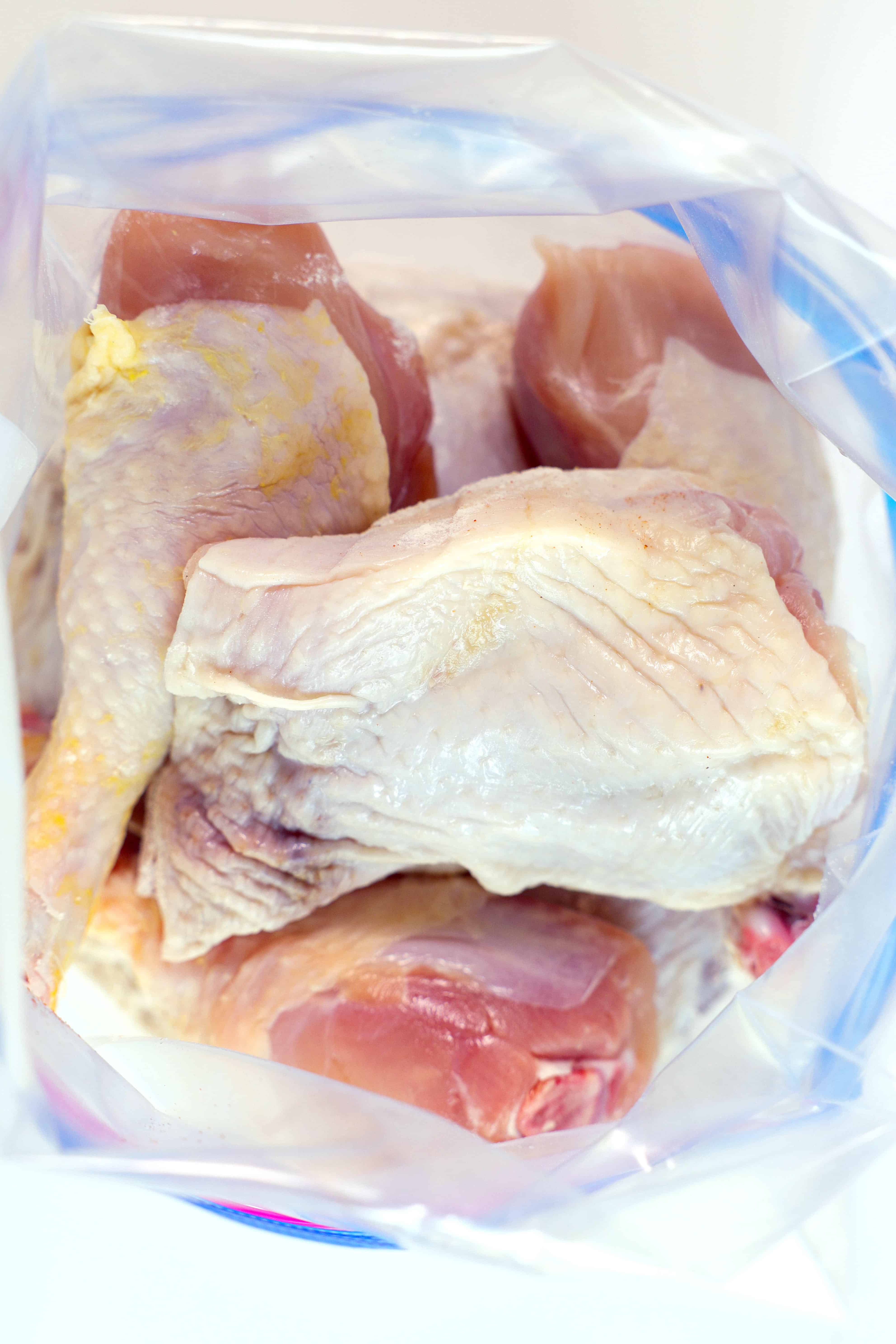 A look down inside a zip-top bag where raw chicken legs and thighs have been added on top of a flour dredge.