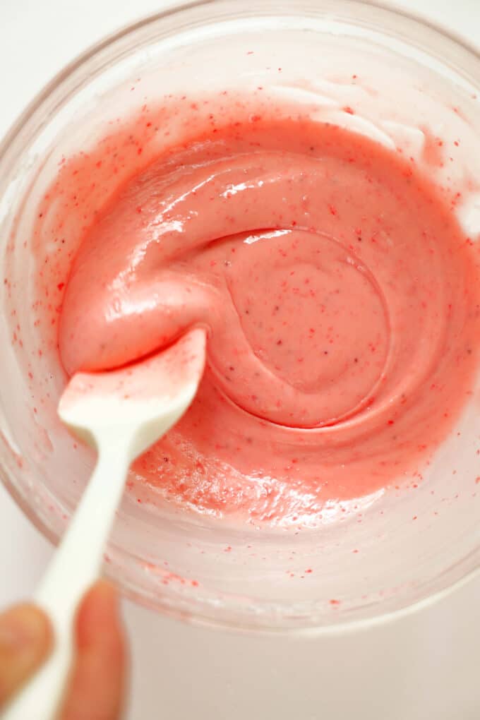 The strawberry glaze being stirred with a silicon spatula in a glass mixing bowl.